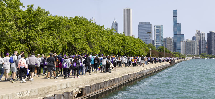 Large crowd of participants walks along the Lake Michigan shoreline with Chicago skyline in background.