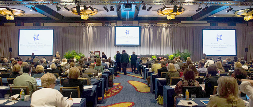 Participants sit in a large meeting room at a conference